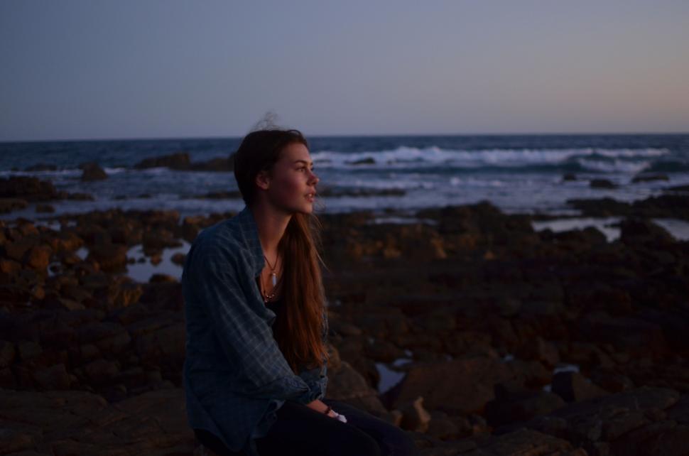 Free Image of Woman Sitting on Rock Near Ocean 