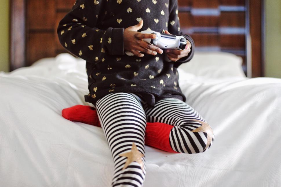 Free Image of Little Girl Sitting on Bed Holding Remote 