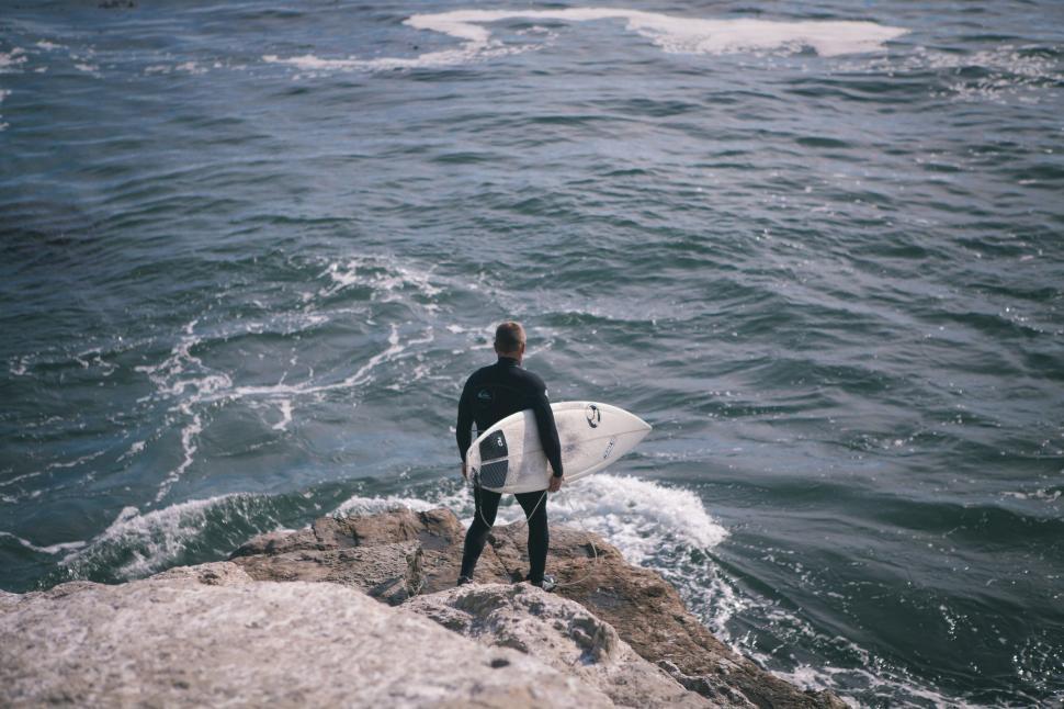 Free Image of Man Standing on Rock With Surfboard 
