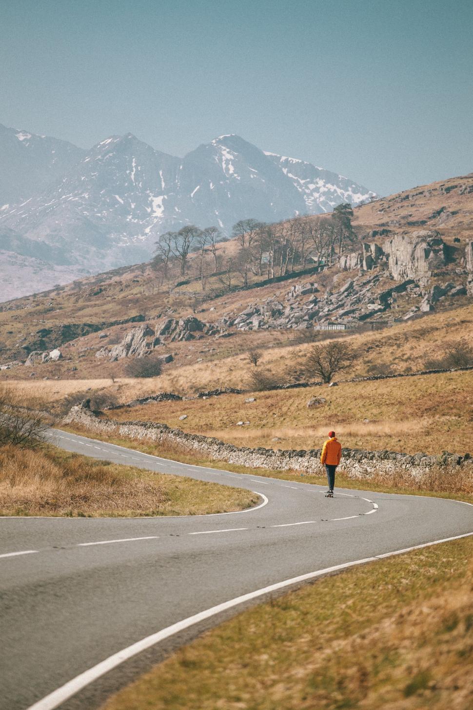Free Image of Person Walking Down Winding Road With Mountains in Background 