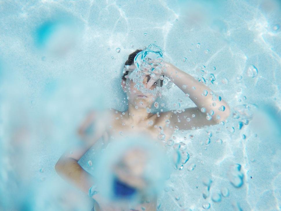 Free Image of Woman Swimming in Blue Pool With Bubbles 