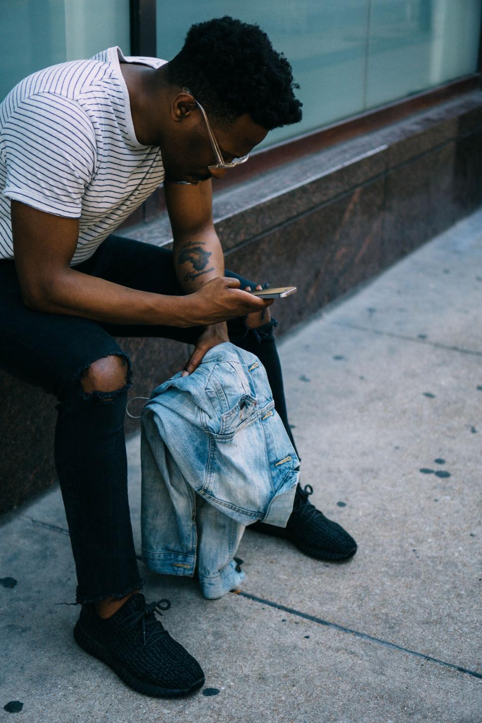 Free Image of Man Sitting on Curb Looking at Cell Phone 