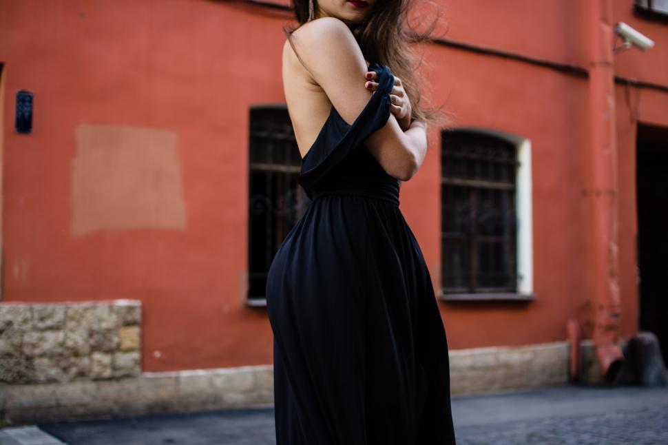 Free Image of Woman in Black Dress Standing in Front of Red Building 