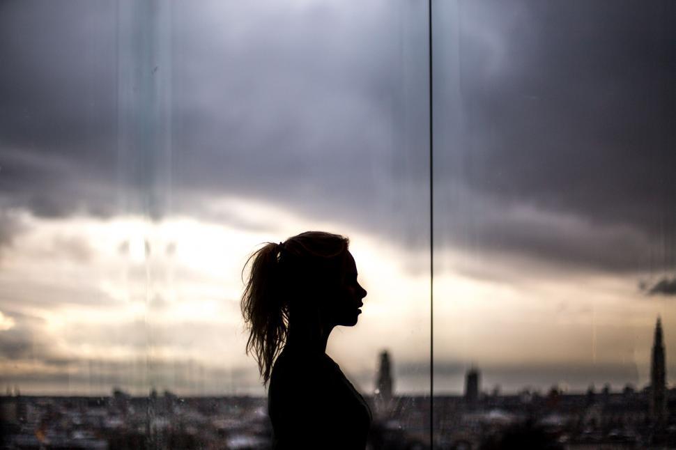 Free Image of Woman Standing in Front of Window With City View 