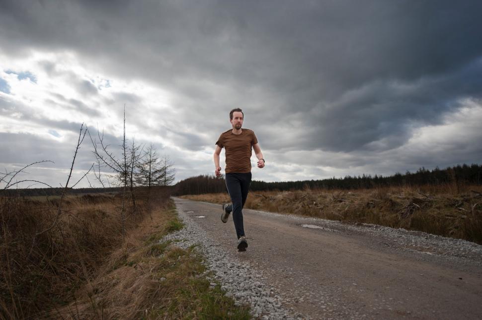 Free Image of Man Running Down Dirt Road Under Cloudy Sky 