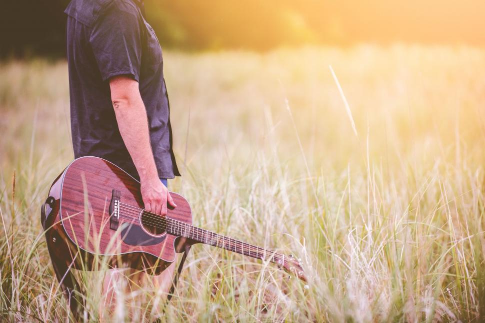 Free Image of Man Standing in Field Holding Guitar 