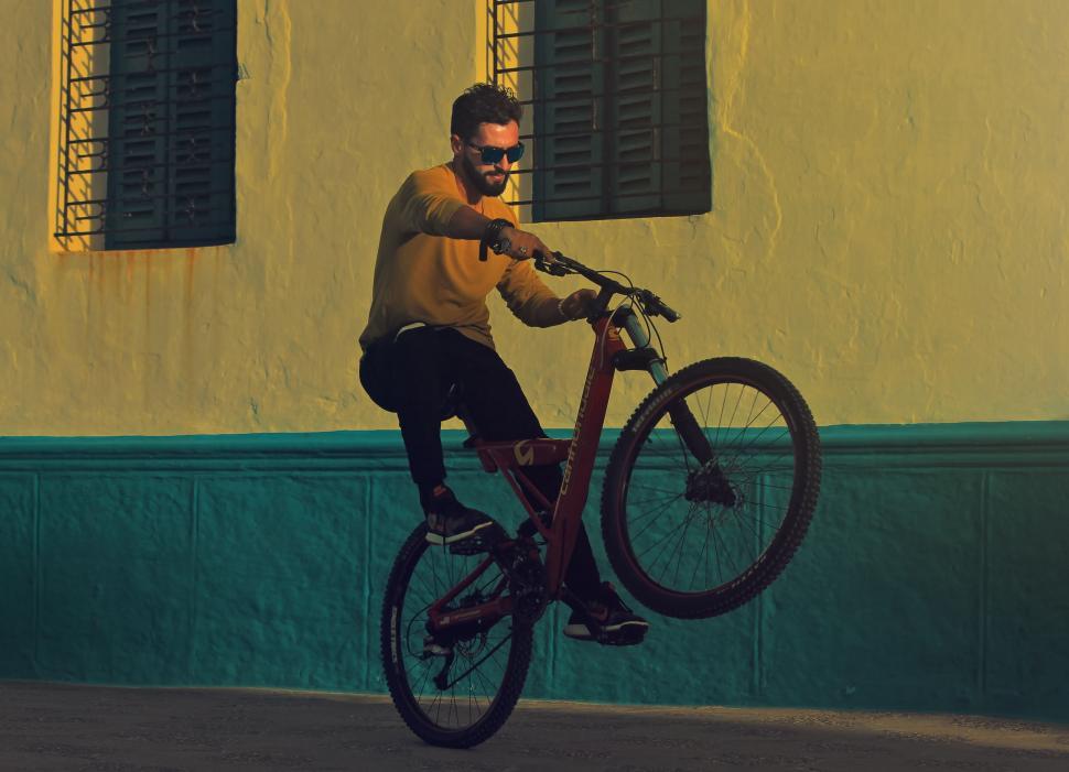 Free Image of Man Riding Bike Down Street Next to Building 