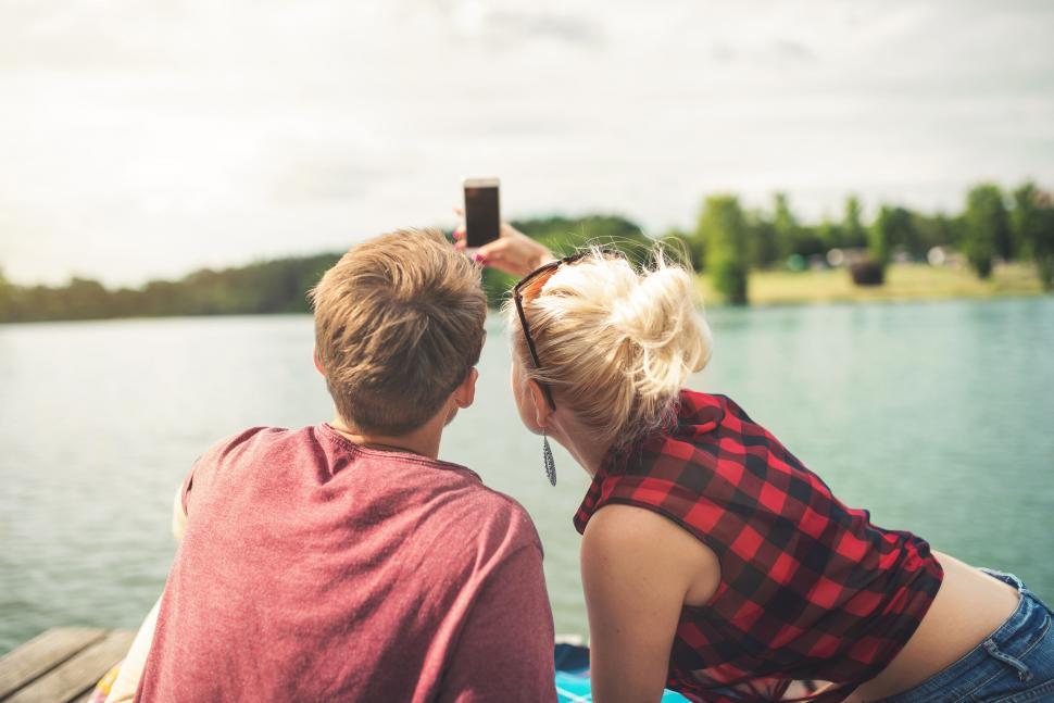 Free Image of Man and Woman Sitting on Dock Taking Picture of Lake 