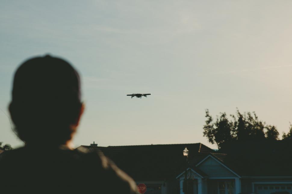 Free Image of Person Standing in Front of House With Plane Flying Overhead 