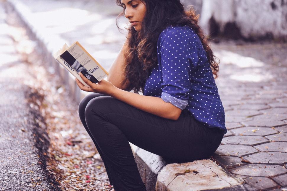 Free Image of Woman Sitting on Curb Reading a Book 