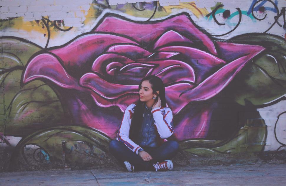 Free Image of Woman Sitting in Front of Wall With Rose Painting 