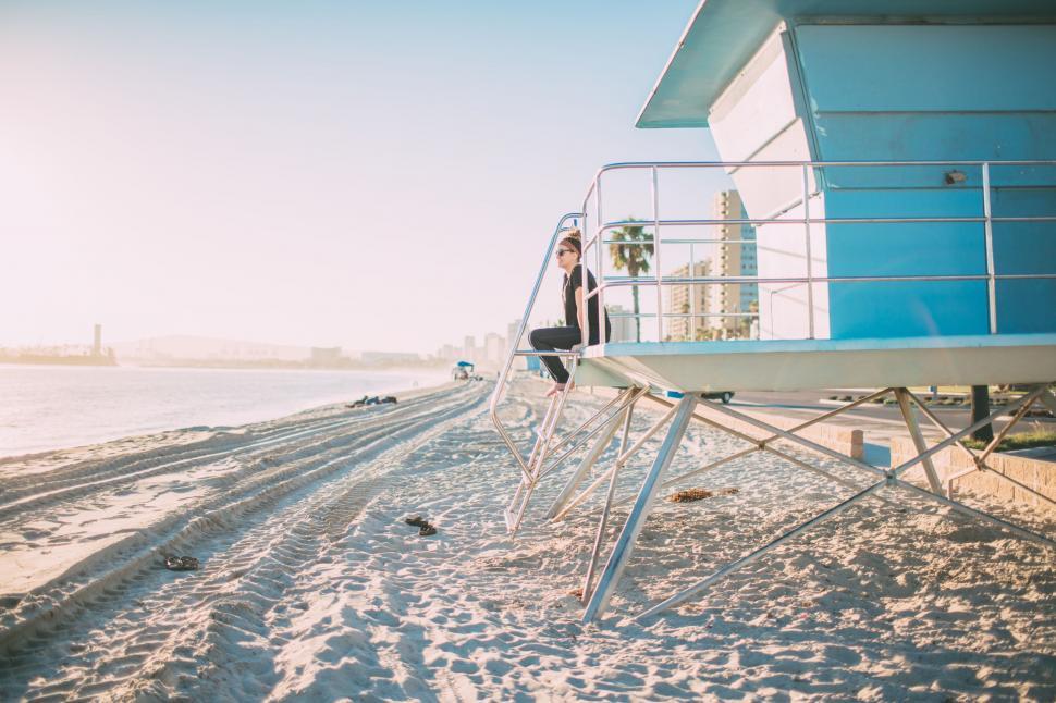 Free Image of Man Sitting Next to Life Guard Chair on Beach 