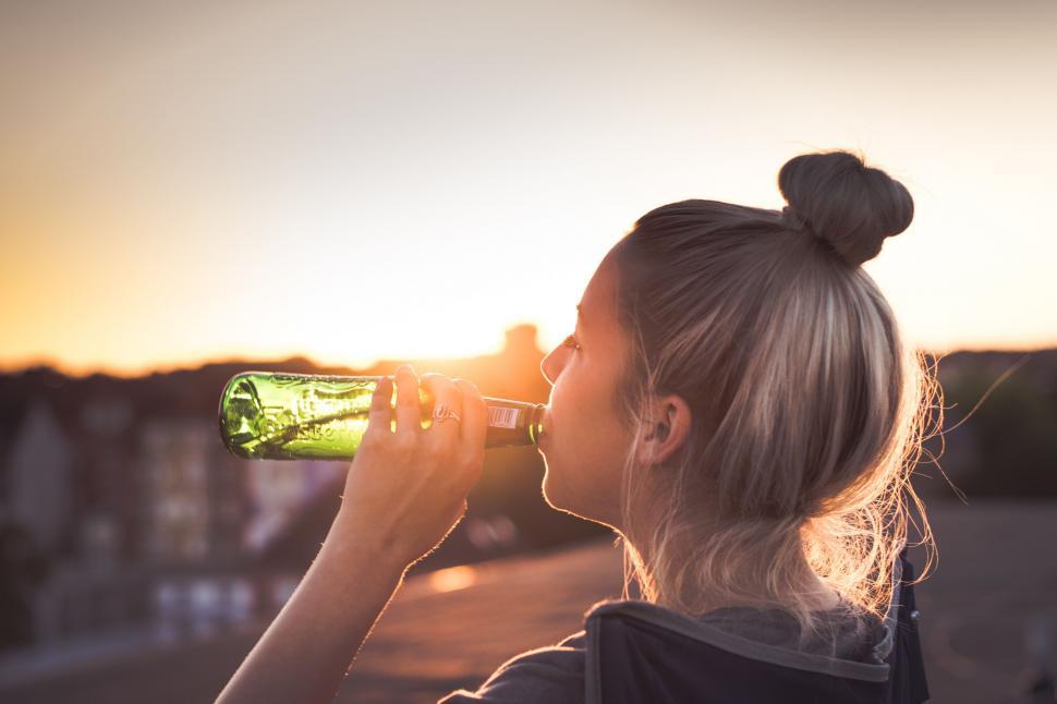 Free Image of Woman Drinking From Green Bottle With Sunset Background 
