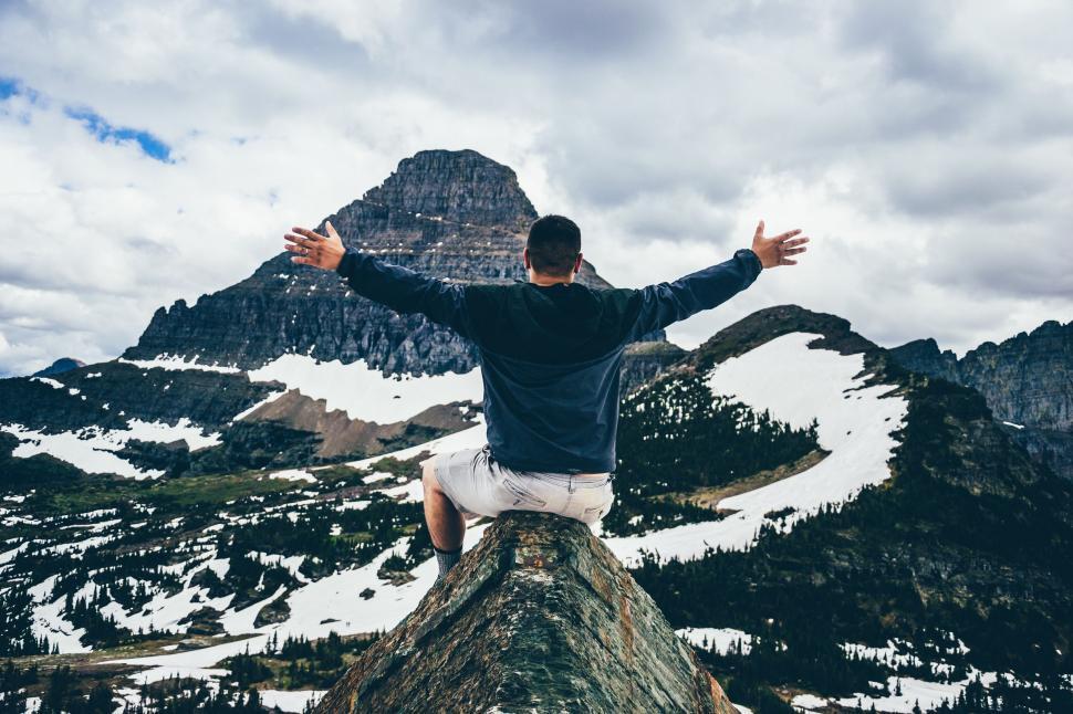 Free Image of Man Sitting on Top of Mountain With Arms Wide Open 