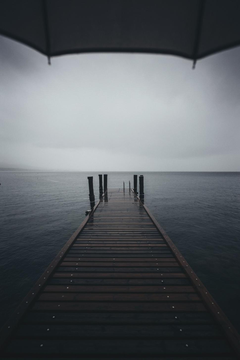 Free Image of Long Pier Extending Into the Ocean Under a Cloudy Sky 