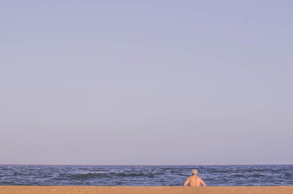 Free Image of Person Sitting on Beach Flying Kite 