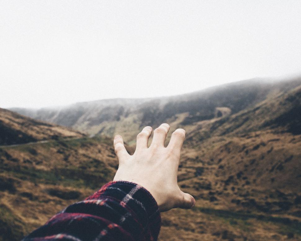 Free Image of Hand Reaching Up Towards Mountains 