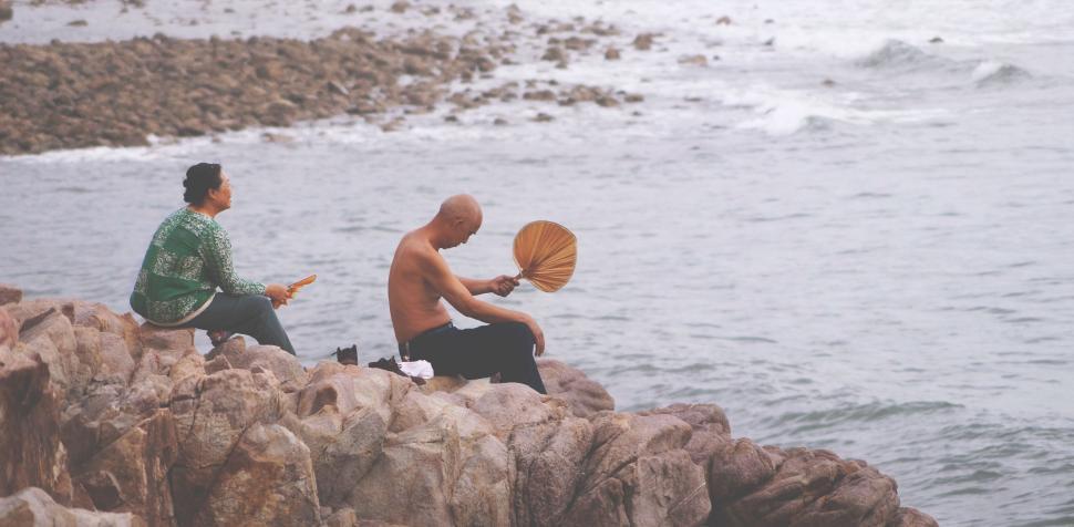 Free Image of Two Men Sitting on Rock by Water 
