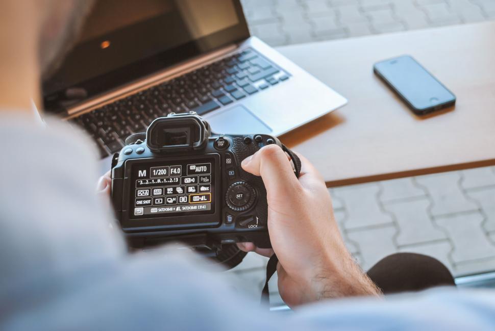 Free Image of Man Holding Camera in Front of Laptop 