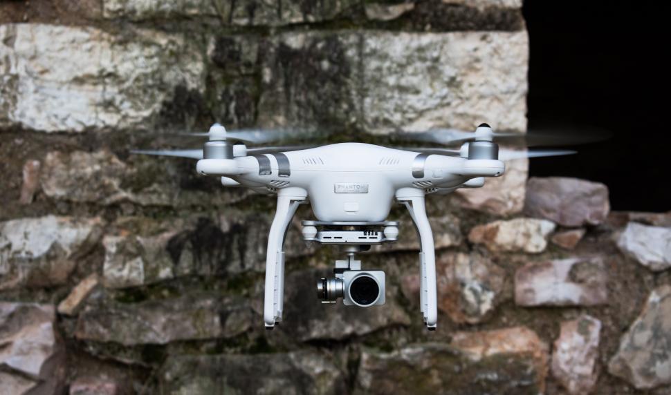 Free Image of Small White Camera Flying Over Stone Wall 