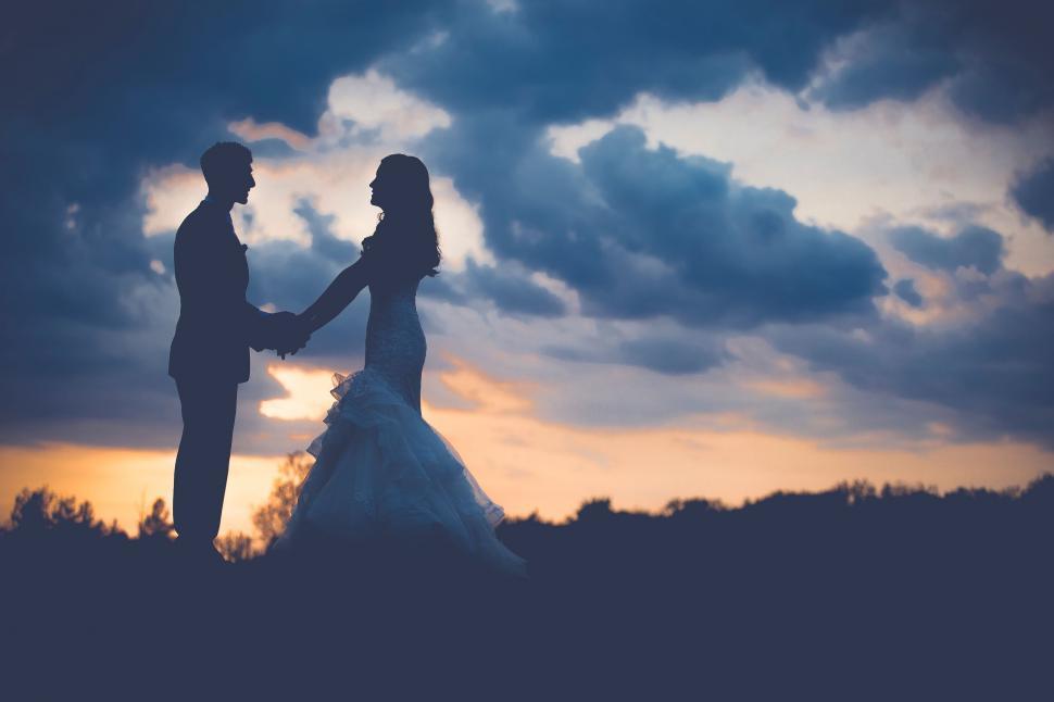 Free Image of Bride and Groom Holding Hands Under Cloudy Sky 
