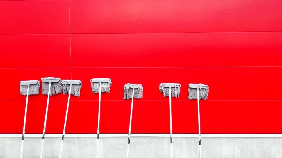 Free Image of Row of Mop Heads Against Red Wall 
