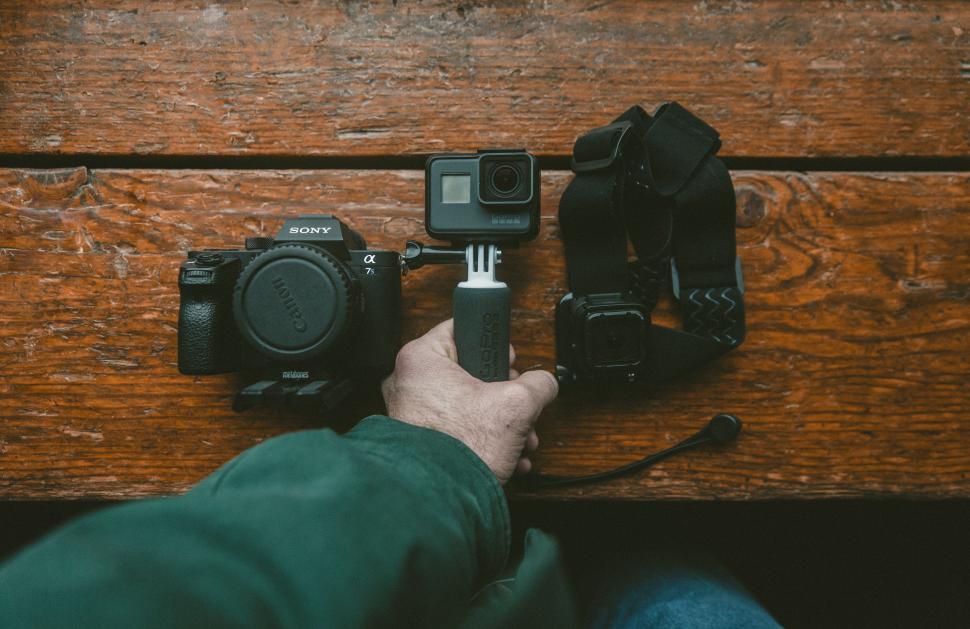 Free Image of Person Holding Camera Next to Wooden Table 