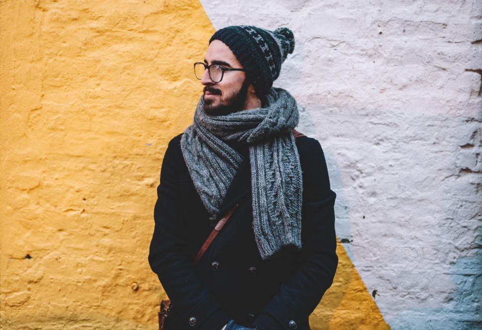 Free Image of Man Wearing Hat and Scarf Standing in Front of Yellow and White Wall 