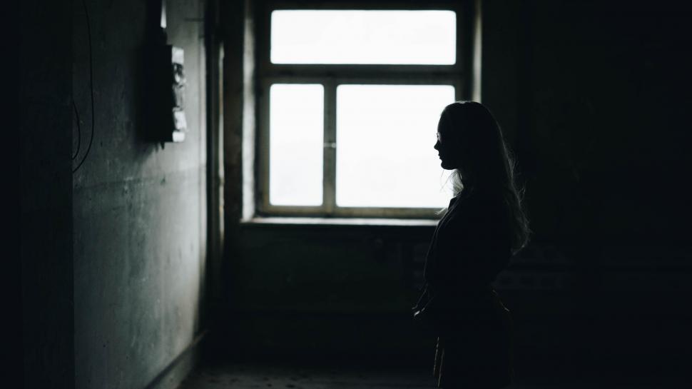Free Image of Woman Standing Next to Window in Dark Room 