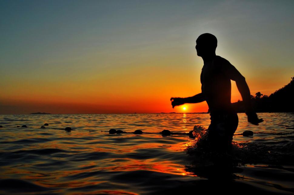 Free Image of Man Walking Into the Ocean at Sunset 