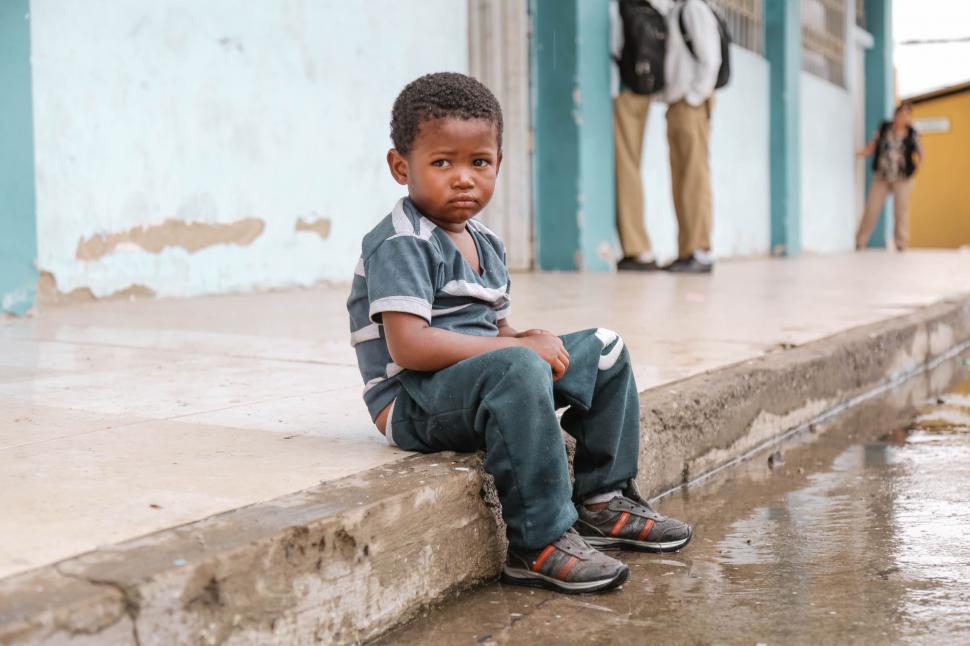 Free Image of Young Boy Sitting on the Curb of a Building 