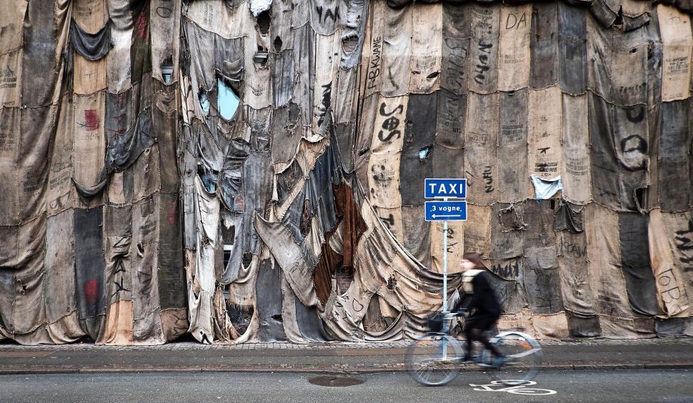 Free Image of Man Riding Bike Past Tall Wooden Building 