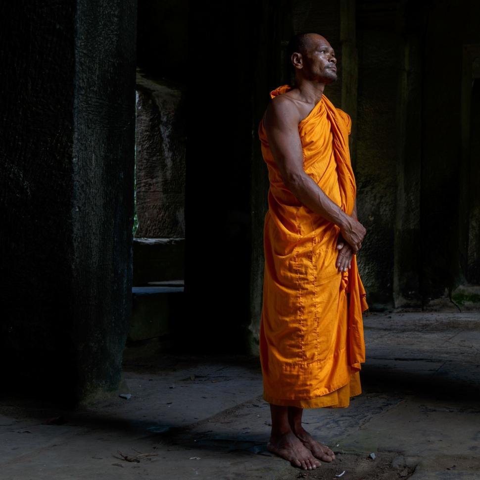 Free Image of Man in Orange Robe Standing in Dark Room 