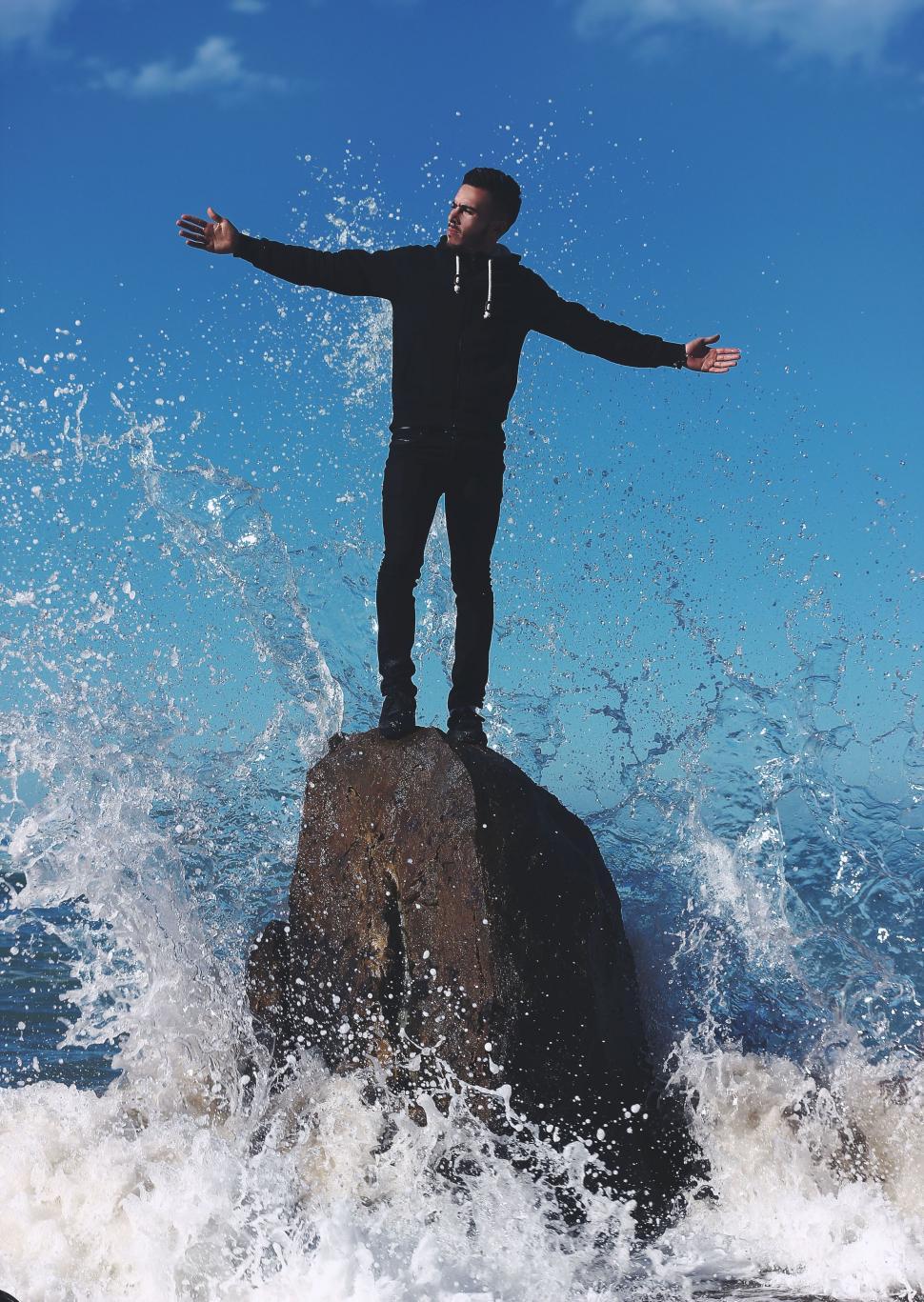 Free Image of Man Standing on Top of Rock in Ocean 