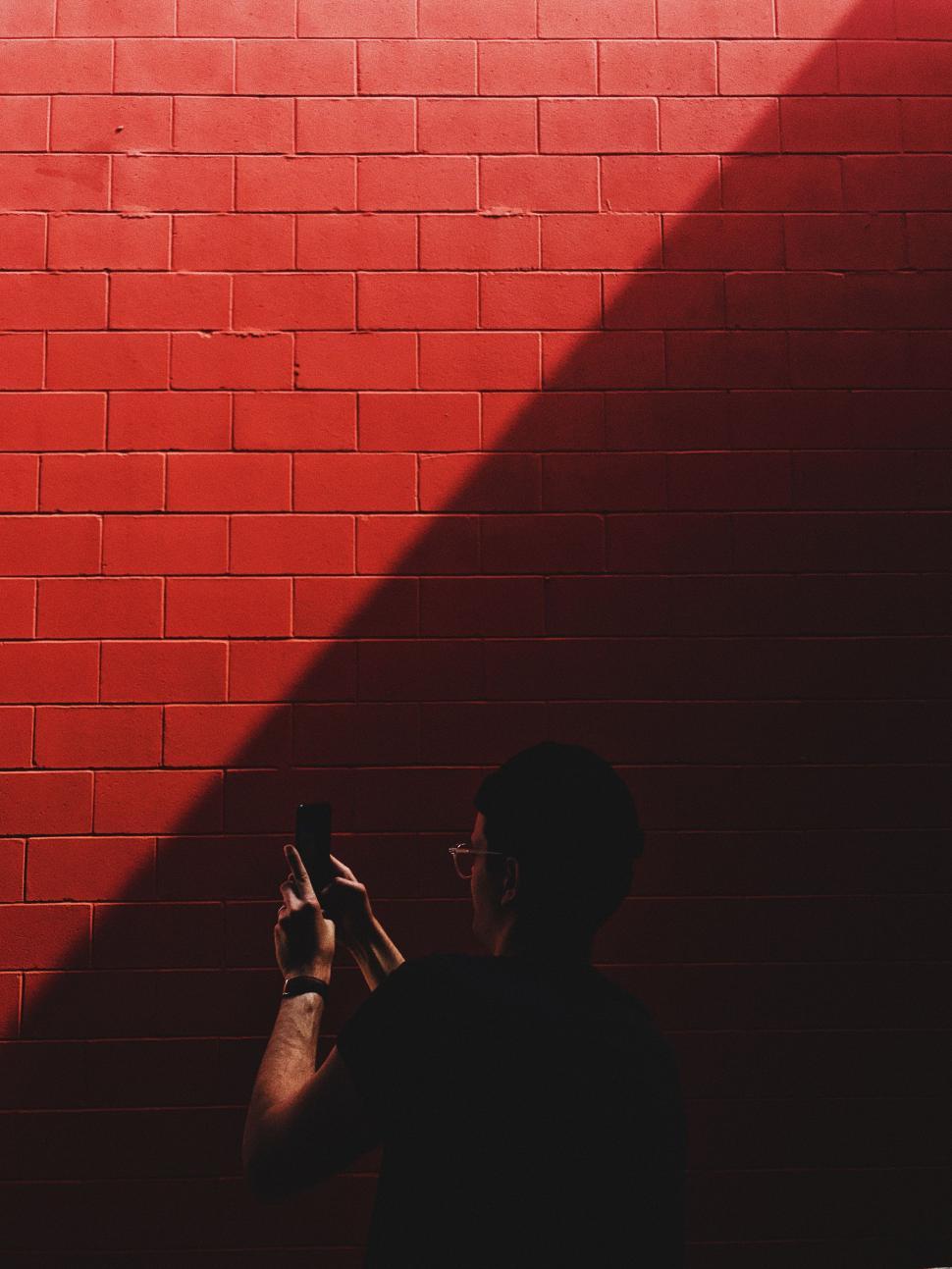 Free Image of Man Standing in Front of Brick Wall Holding Cell Phone 