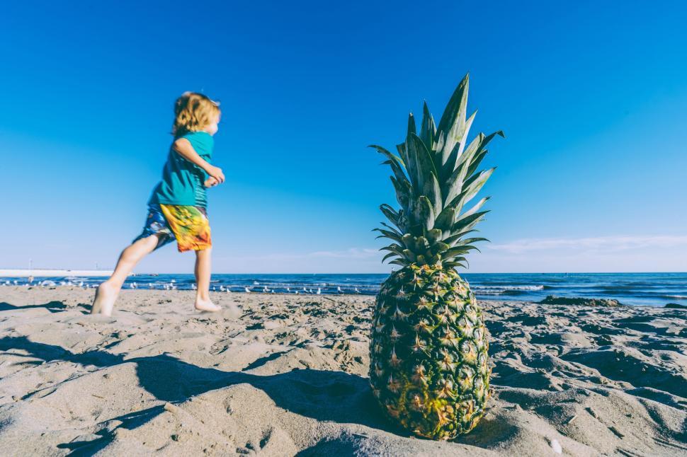 Free Image of Little Girl Standing on Sandy Beach Next to Pineapple 