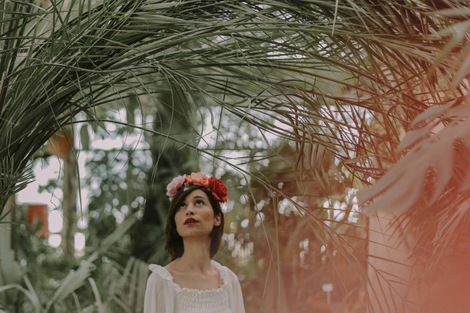 Free Image of Woman Standing Under Palm Tree With Flower in Hair 