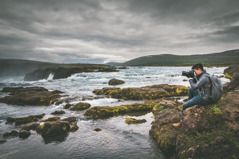 Free Image of Man Sitting on Rock With Camera 