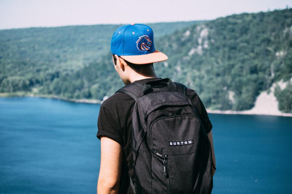 Free Image of Man With Blue Hat and Backpack Looking Over Lake 