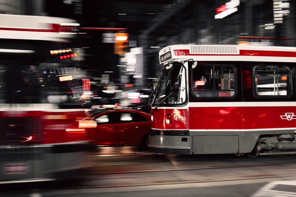 Free Image of Red and White Bus Driving Next to Red Car on Street 