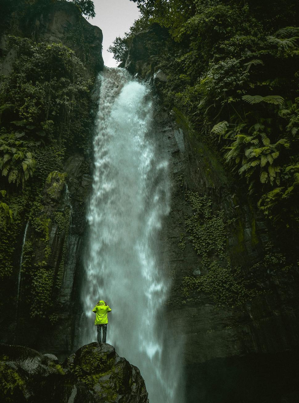 Free Image of Person in Yellow Jacket Standing in Front of Waterfall 