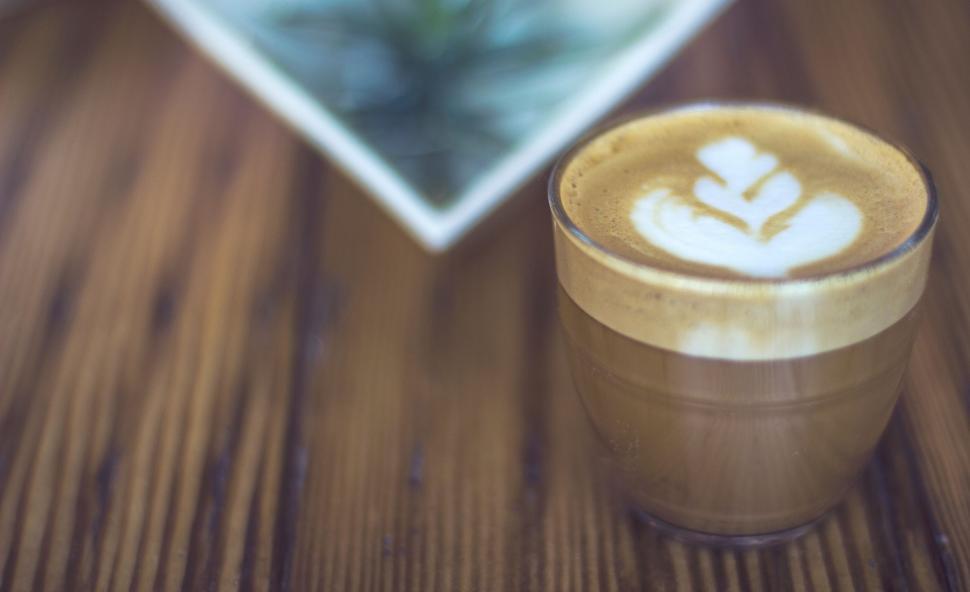 Free Image of A Cappuccino on a Wooden Table With a Picture in the Background 