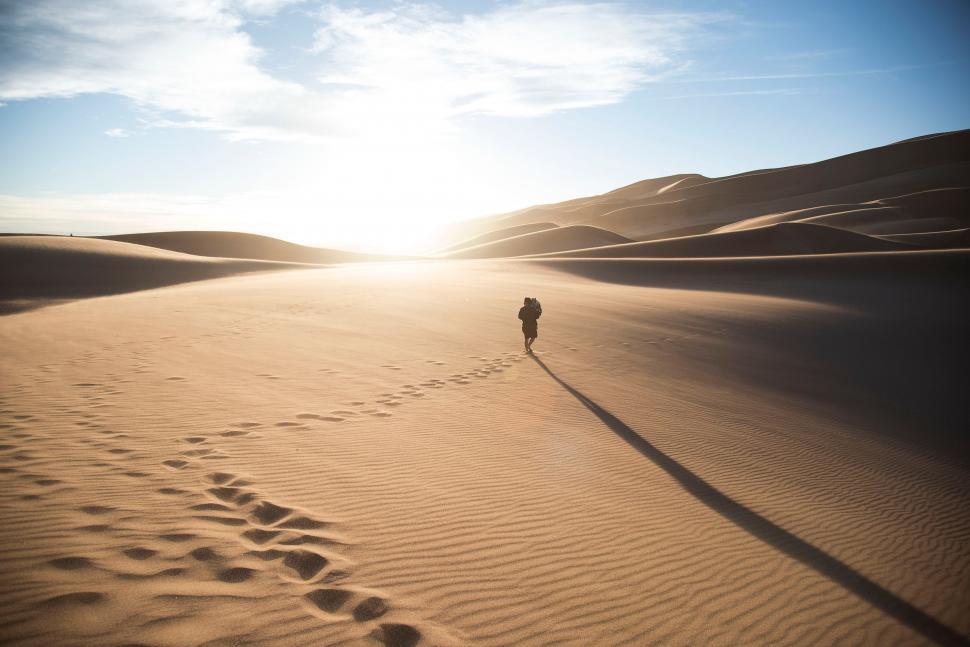 Free Image of Person Walking Across Sandy Field at Sunset 