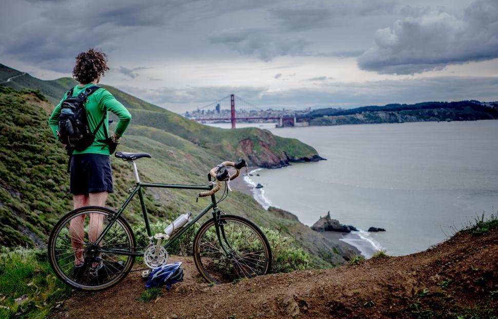 Free Image of Man Standing Next to Bike on Hilltop 