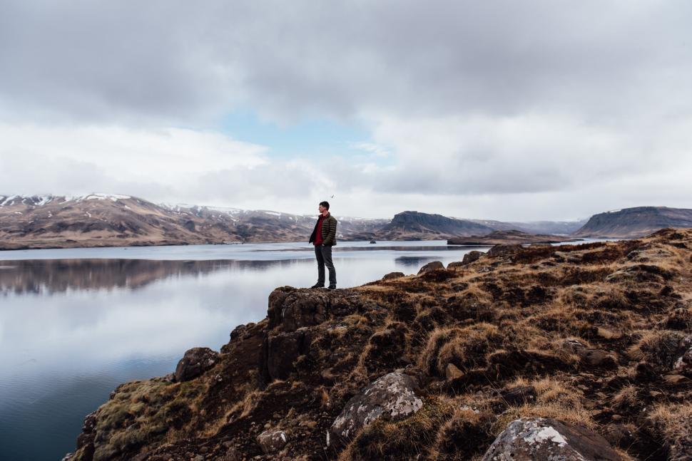 Free Image of Man Standing on Top of a Mountain Next to a Lake 
