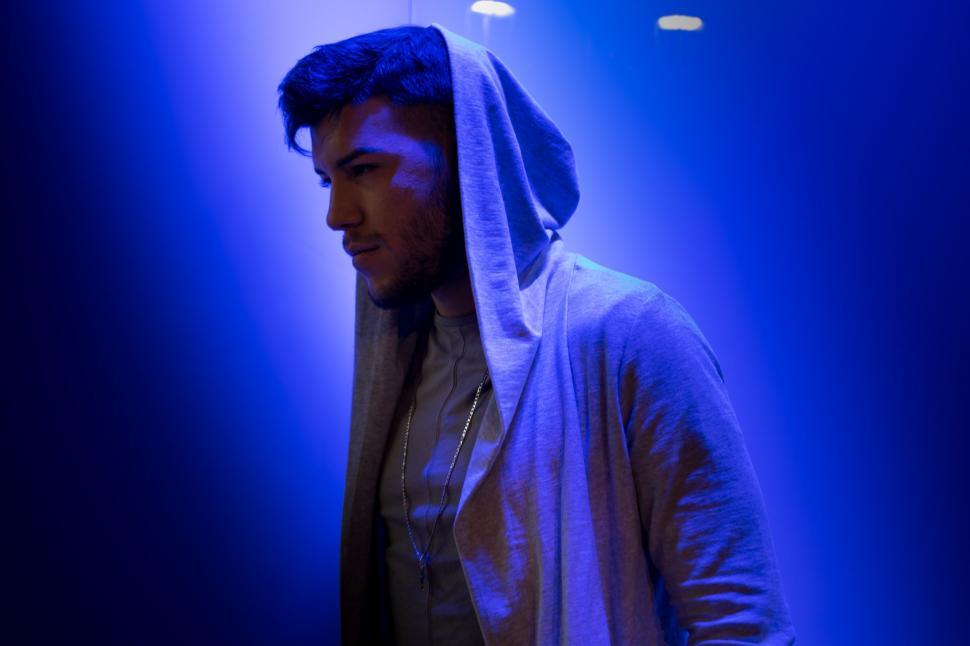 Free Image of Man in Hoodie Standing in Front of Blue Light 
