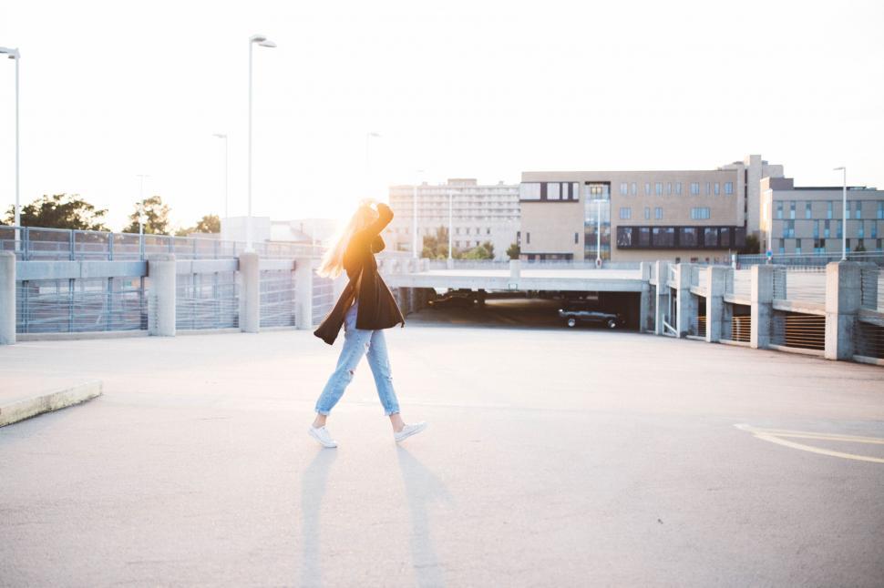 Free Image of Woman Walking Across Parking Lot Next to Tall Buildings 