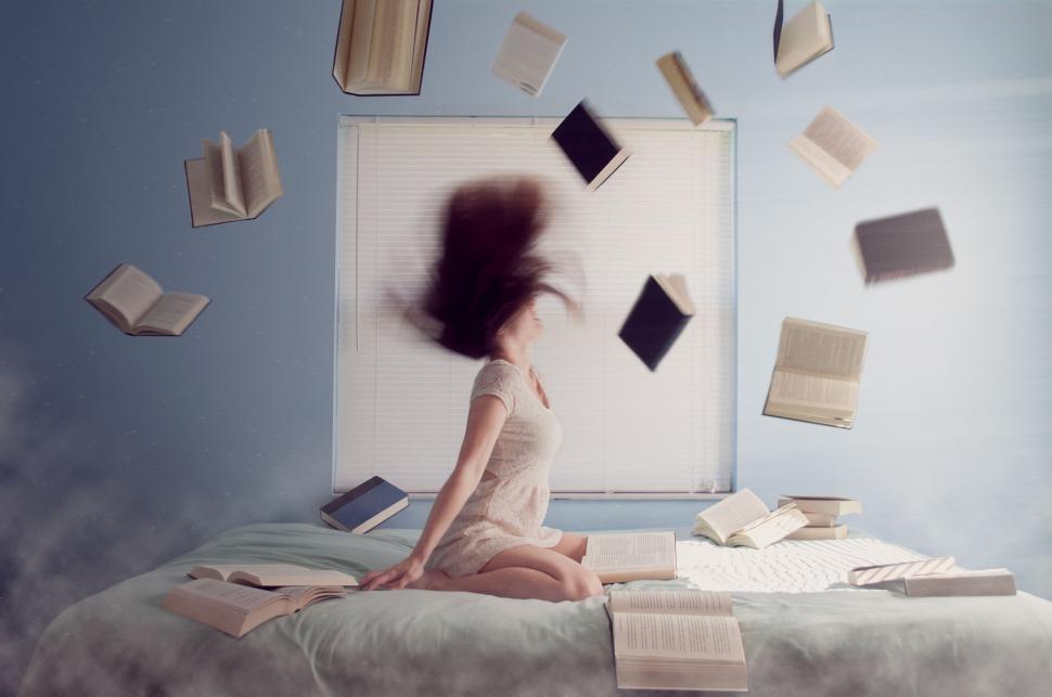Free Image of Woman Sitting on Bed With Flying Books 