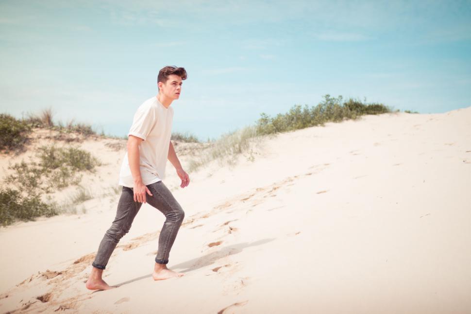 Free Image of Young Man Walking Across Sandy Beach 