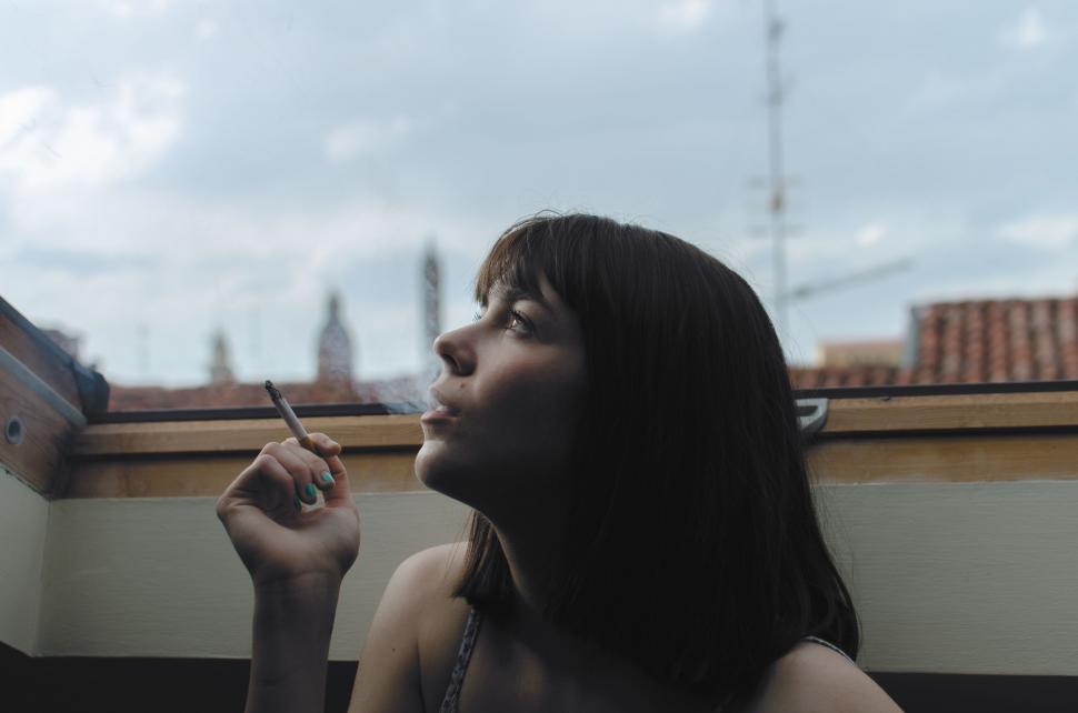 Free Image of Woman Smoking a Cigarette in Front of a Window 